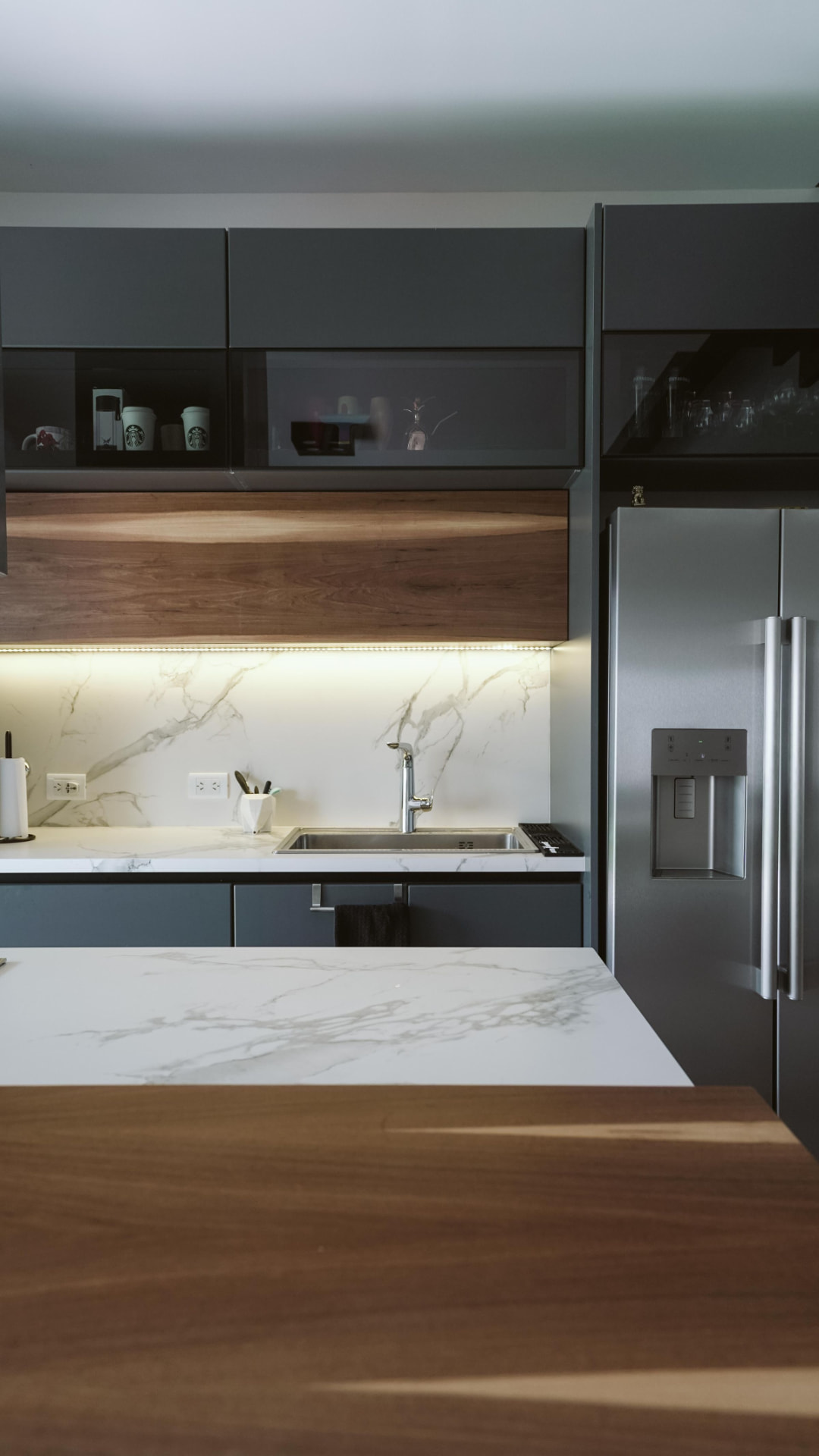 Charcoal cabinetry with a walnut island and marble-pattern countertop