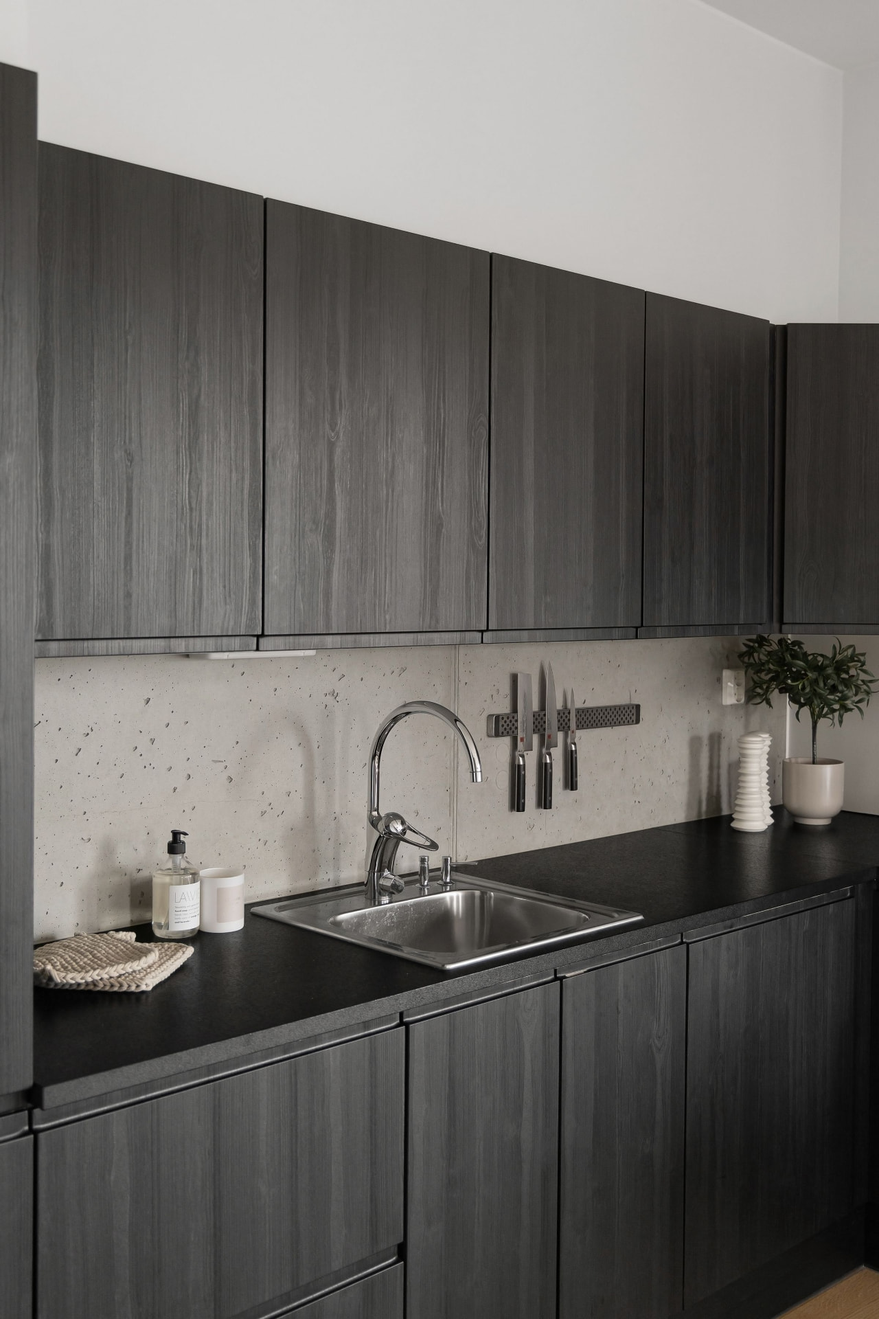 Charcoal wood-grain frameless cabinets with a black countertop and concrete backsplash